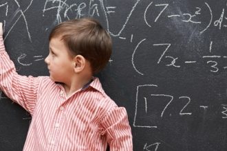 boy in a striped polo pointing at a blackboard