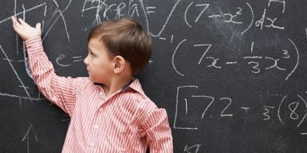 boy in a striped polo pointing at a blackboard