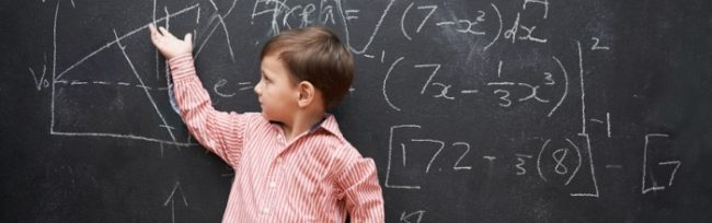 boy in a striped polo pointing at a blackboard