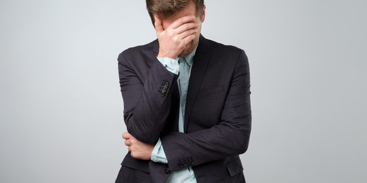 Feeling depressed concept. Exhausted young man in suit covering face with hand